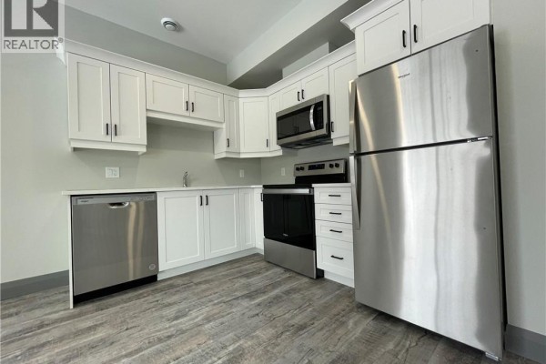 Modern kitchen with white cabinets, stainless steel appliances, and grey wood-look flooring. - 600 Norfolk Street Unit# 303, Simcoe