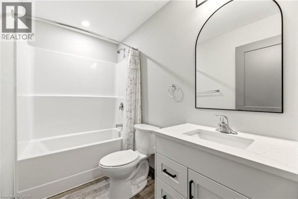 Contemporary bathroom with a white vanity, toilet, bathtub, shower curtain, and arched mirror. - 600 Norfolk Street Unit# 303, Simcoe