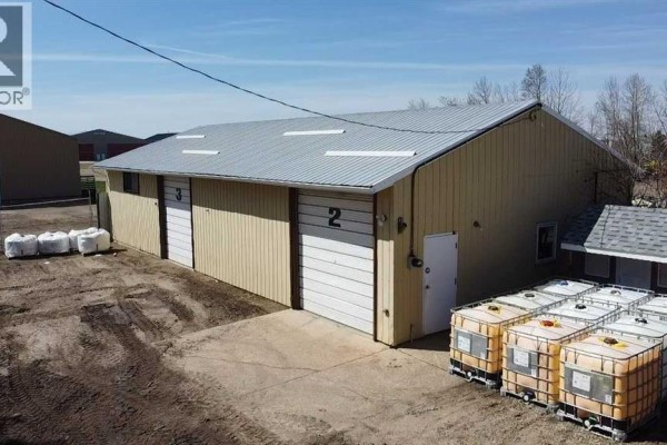 Aerial view of a tan industrial building with multiple windows, a white metal roof, and a gravel parking area. - 6001 40 Avenue, Wetaskiwin