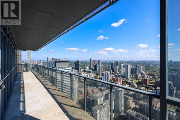 Wide balcony with glass railings offering a panoramic view of a dense city skyline under a blue sky. - 6005 - 7 Grenville Street, Toronto