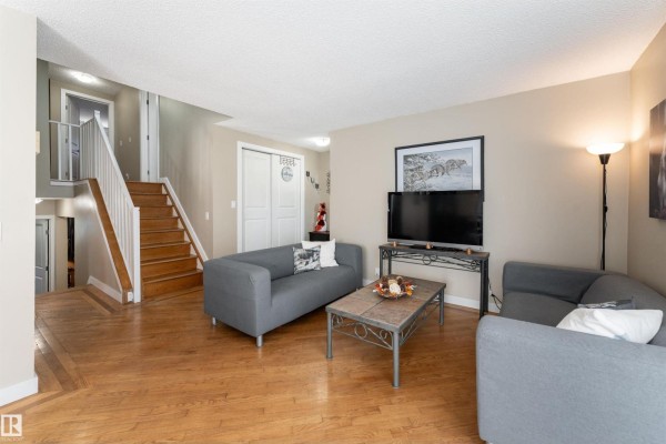 Living room with two gray sofas, hardwood floors, a television, and a view of a staircase and hallway. - 6007 37 Av Nw, Edmonton