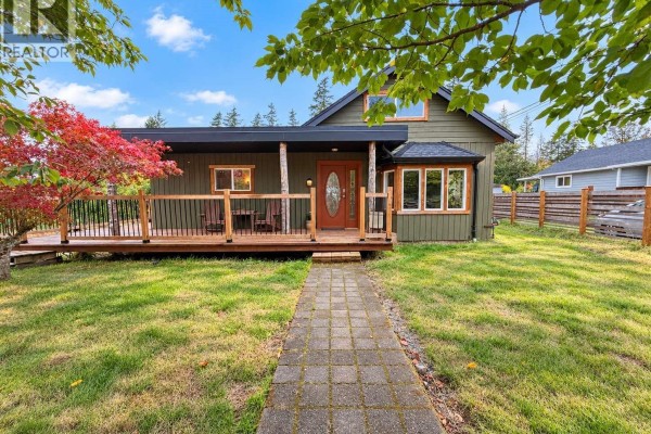 View of the green house exterior from the driveway, showing the covered porch and wooden deck. - 6008 Grandview Rd, Port Alberni