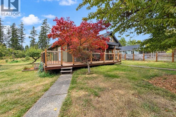 Side view of the house with a wraparound deck, grassy yard, and mature trees. - 6008 Grandview Rd, Port Alberni