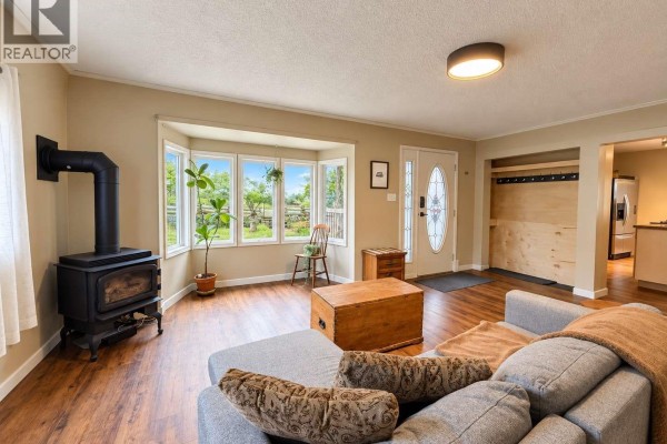 Living room with a wood stove, bay window overlooking the yard, and a grey sectional sofa. - 6008 Grandview Rd, Port Alberni