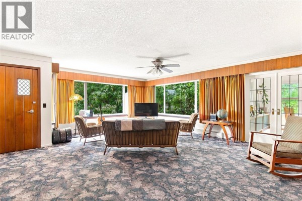 Living room with patterned carpet, large windows, and wooden doors. - 6009 River Rd, Port Alberni