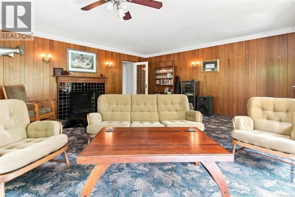 Living room with fireplace, wood paneling, and plush furniture. - 6009 River Rd, Port Alberni