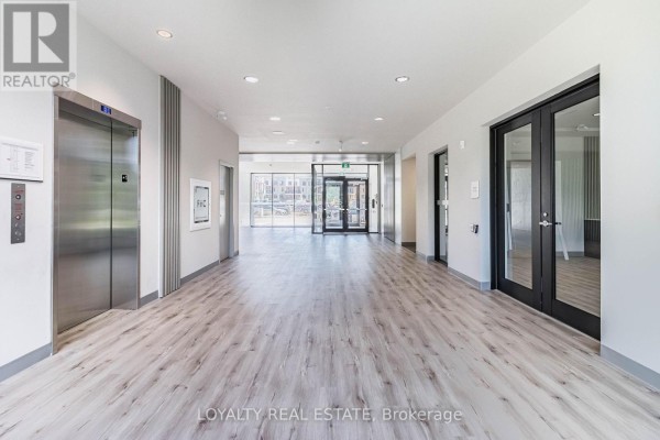 Wide apartment building hallway with elevators and light wood laminate flooring. - 601 - 103 Rogers Street, Waterloo