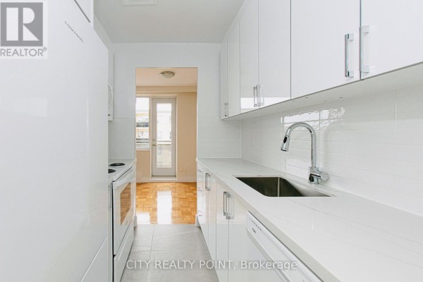 Galley kitchen with white cabinets, quartz countertops, stainless steel sink, and backsplash. - 601 - 2 Grandstand Place, Toronto