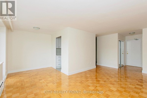 Living area with polished parquet floors, white walls, and a view into the kitchen area. - 601 - 2 Grandstand Place, Toronto