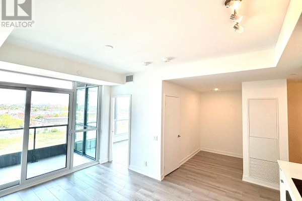 Open concept living area with light wood floors, white walls, and a view of the balcony. - 601 - 20 Deans Drive, Toronto