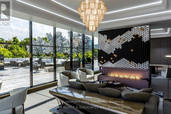 Contemporary lounge area with a dramatic chandelier, fireplace, and floor-to-ceiling windows overlooking an outdoor patio. - 601 - 2450 Bloor Street W, Toronto