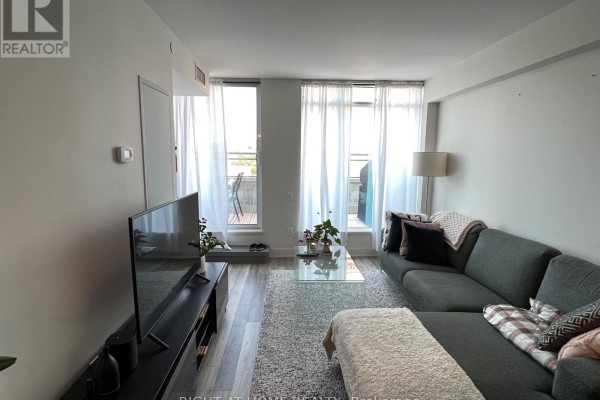 Living room with sectional sofa, coffee table, television, and large windows with sheer curtains. - 601 - 411 Mackay Street, Ottawa