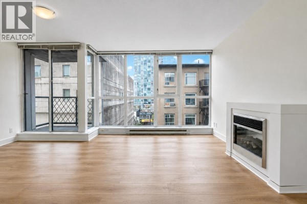 Living room with light wood floors, large windows, and a modern electric fireplace. - 601 1199 Seymour Street, Vancouver