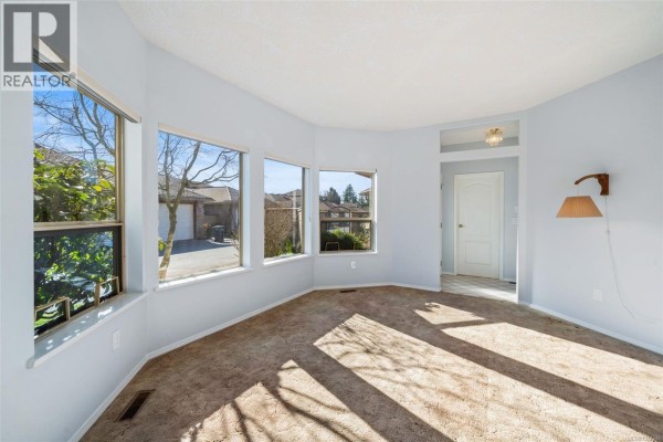 Living room with bay windows overlooking the exterior and carpeted floor. - 601 4515 Pipeline Rd, Saanich