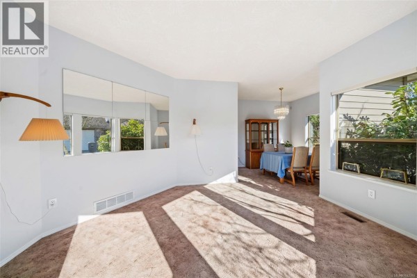 Living and dining area with carpet, a mirrored wall, and a wooden dining set. - 601 4515 Pipeline Rd, Saanich