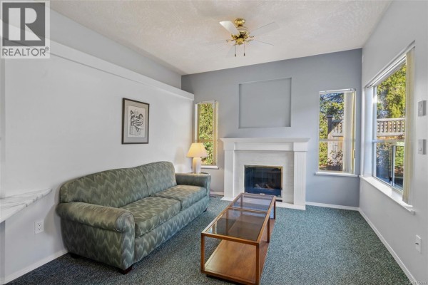 Living room with a green sofa, coffee table, fireplace, and windows. - 601 4515 Pipeline Rd, Saanich