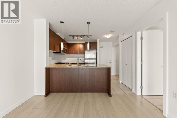 Interior view of a kitchen with dark wood cabinets, granite countertops, and stainless steel appliances. - 601 9868 Cameron Street, Burnaby