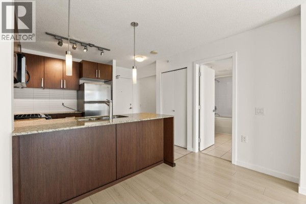 View of the kitchen showing dark wood cabinets, granite countertops, and an open doorway to a bathroom. - 601 9868 Cameron Street, Burnaby