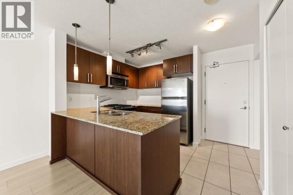 Kitchen with dark wood cabinets, granite island, stainless steel refrigerator, and beige tiled floor. - 601 9868 Cameron Street, Burnaby
