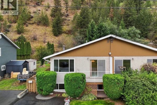 Side view of a beige duplex with adjacent grey siding duplex and storage sheds. - 6011 Dallas Drive, Kamloops
