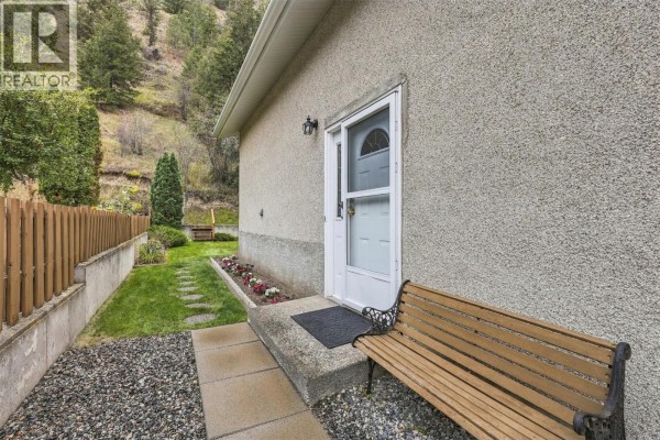 Front entrance of a duplex with a white door, bench, and gravel pathway. - 6011 Dallas Drive, Kamloops