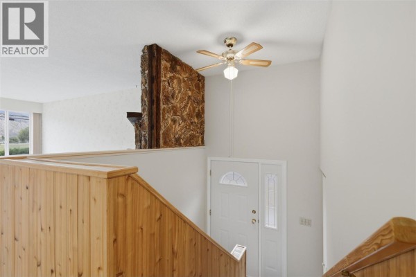 Interior entryway with a wood railing, stone accent wall, and white front door. - 6011 Dallas Drive, Kamloops