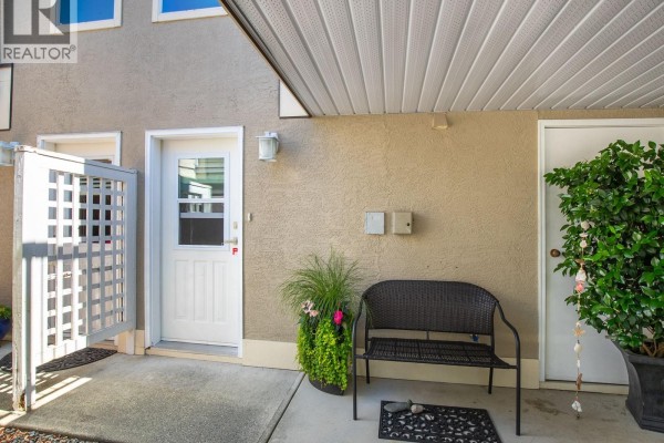 Covered entryway with a white door, outdoor seating, and potted plants. - 6012 Jake's Pl, Nanaimo