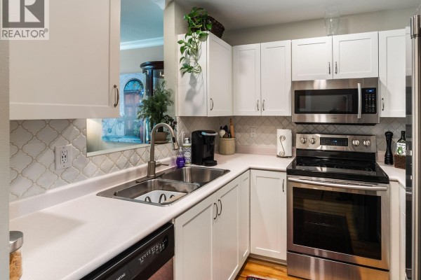 White kitchen with light-colored backsplash, stainless steel appliances, and a double sink. - 6012 Jake's Pl, Nanaimo