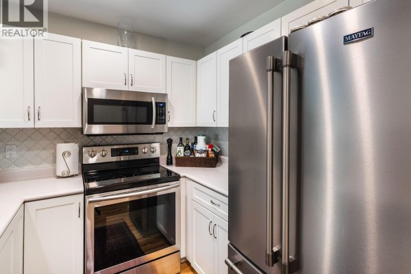 View of a stainless steel refrigerator and white cabinets in the kitchen area. - 6012 Jake's Pl, Nanaimo