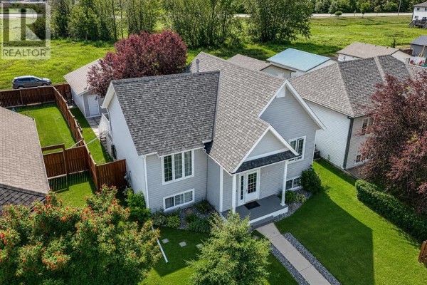Aerial view of a grey house with a fenced backyard, garage, and surrounding trees. - 6015 50 A Street, Ponoka