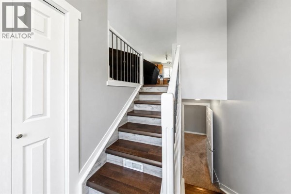 Interior view of a staircase with dark wood treads, white risers, and metal railings. - 6015 50 A Street, Ponoka