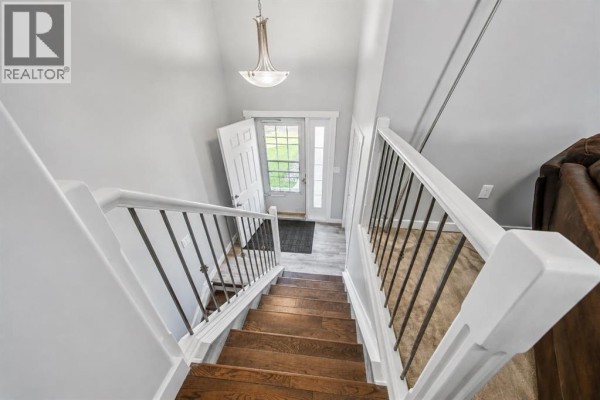 Looking down a wooden staircase from the upper level into the entryway and front door. - 6015 50 A Street, Ponoka