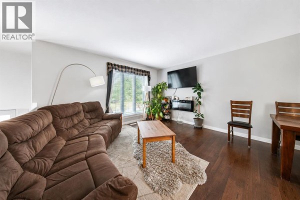 Living room with a large brown sectional sofa, coffee table, dining table, and television. - 6015 50 A Street, Ponoka