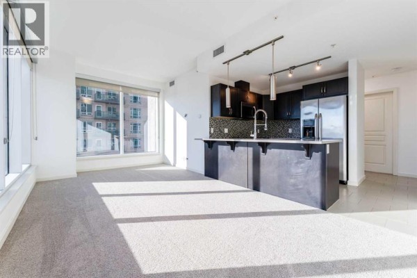 Open living area with large windows and modern kitchen - 602, 1320 1 Street Se, Calgary