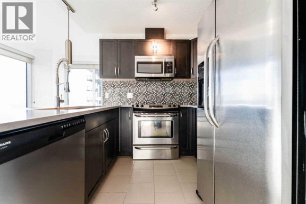 Compact kitchen featuring dark cabinetry and tile backsplash - 602, 1320 1 Street Se, Calgary