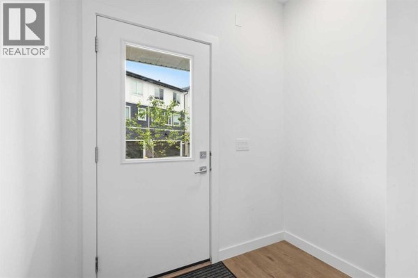 Interior hallway with a white door, wood floor, and a closet. - 602, 335 Creekside Boulevard Sw, Calgary