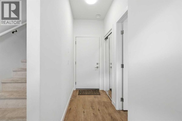 Empty room with white walls, wood floors, a framed picture, and a desk. - 602, 335 Creekside Boulevard Sw, Calgary