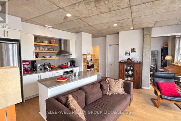 Open concept kitchen and living area with a brown sofa and concrete ceiling. - 602 - 1000 Wellington Street W, Ottawa