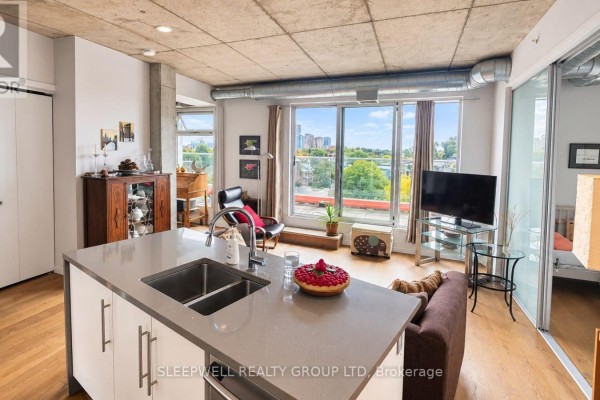 Living area with large windows, city view, and a kitchen island with sink. - 602 - 1000 Wellington Street W, Ottawa