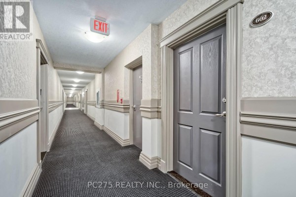 A long, carpeted apartment hallway with patterned wallpaper and gray doors, including unit 602. - 602 - 1030 Coronation Drive, London North