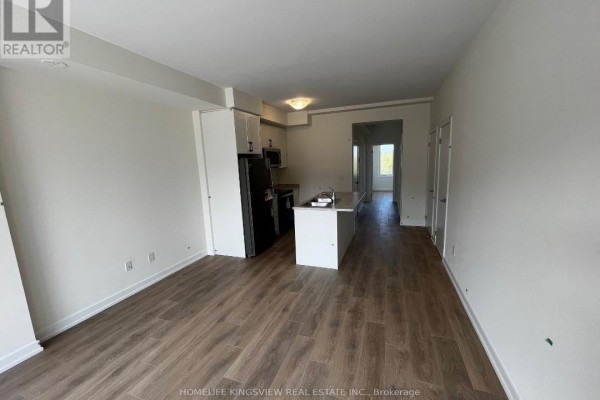 Open concept living area with light wood-look flooring, white walls, and a central kitchen island. - 602 - 160 Densmore Road, Cobourg