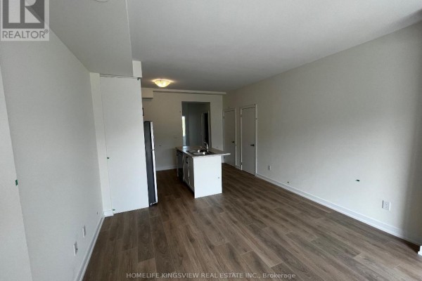 View of an empty living and kitchen area with modern appliances and light wood-look flooring. - 602 - 160 Densmore Road, Cobourg