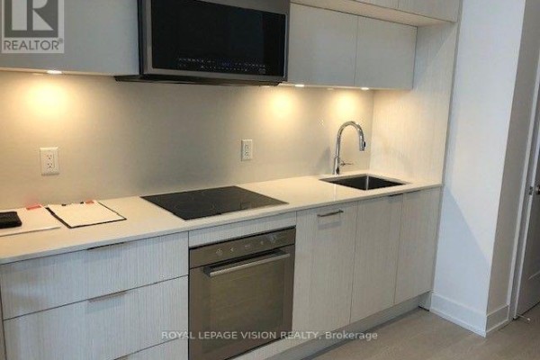 Compact kitchen with light wood cabinets, stainless steel appliances, and under-cabinet lighting. - 602 - 25 Adra Grado Way, Toronto