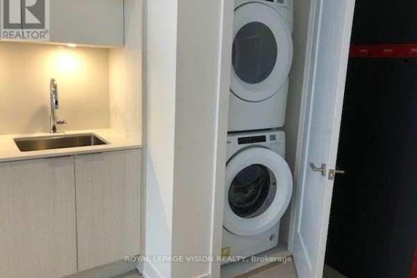 Stacked white washer and dryer units inside a closet with a small sink nearby. - 602 - 25 Adra Grado Way, Toronto
