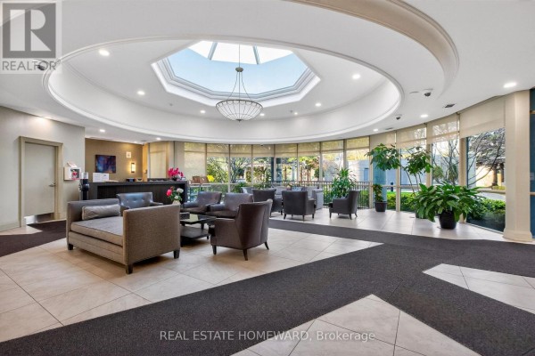 Apartment building lobby with seating area, reception desk, and large skylight. - 602 - 30 Harrison Garden Boulevard, Toronto