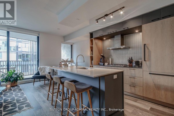 Kitchen island with sink, waterfall countertop, and bar stools, adjacent to cabinetry and appliances. - 602 - 41 Dovercourt Road, Toronto