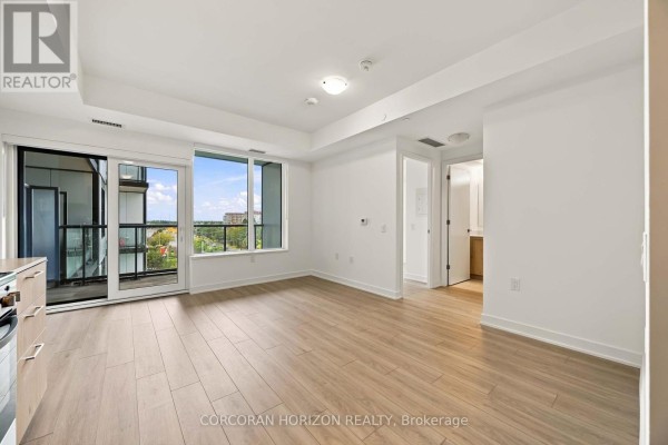 Living area with light wood laminate flooring, large window, and access to a balcony. - 602 - 7437 Kingston Road, Toronto