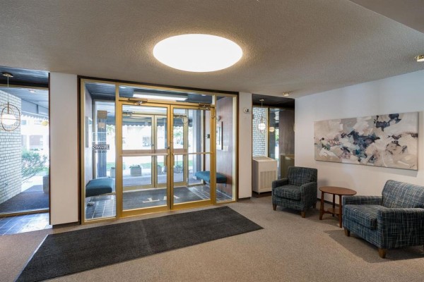 Apartment building lobby with glass doors, seating, and abstract art. - 602 250 Wellington Crescent, Winnipeg