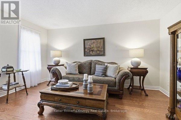 Living room with a sofa, ornate coffee table, hardwood floors, and large windows. - 602 Carlisle Street, Cobourg