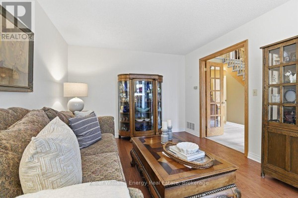 Living room with a sofa, display cabinet, hardwood floors, and view of the staircase. - 602 Carlisle Street, Cobourg